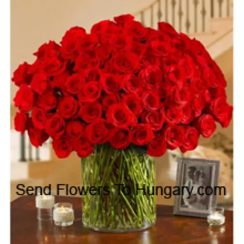 101 rode rozen met wat varens in een grote glazen vaas